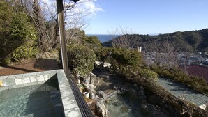 A view of a garden with a pond, surrounded by trees and a distant cityscape. - Hotel Chobo Sanso (Yugawara)