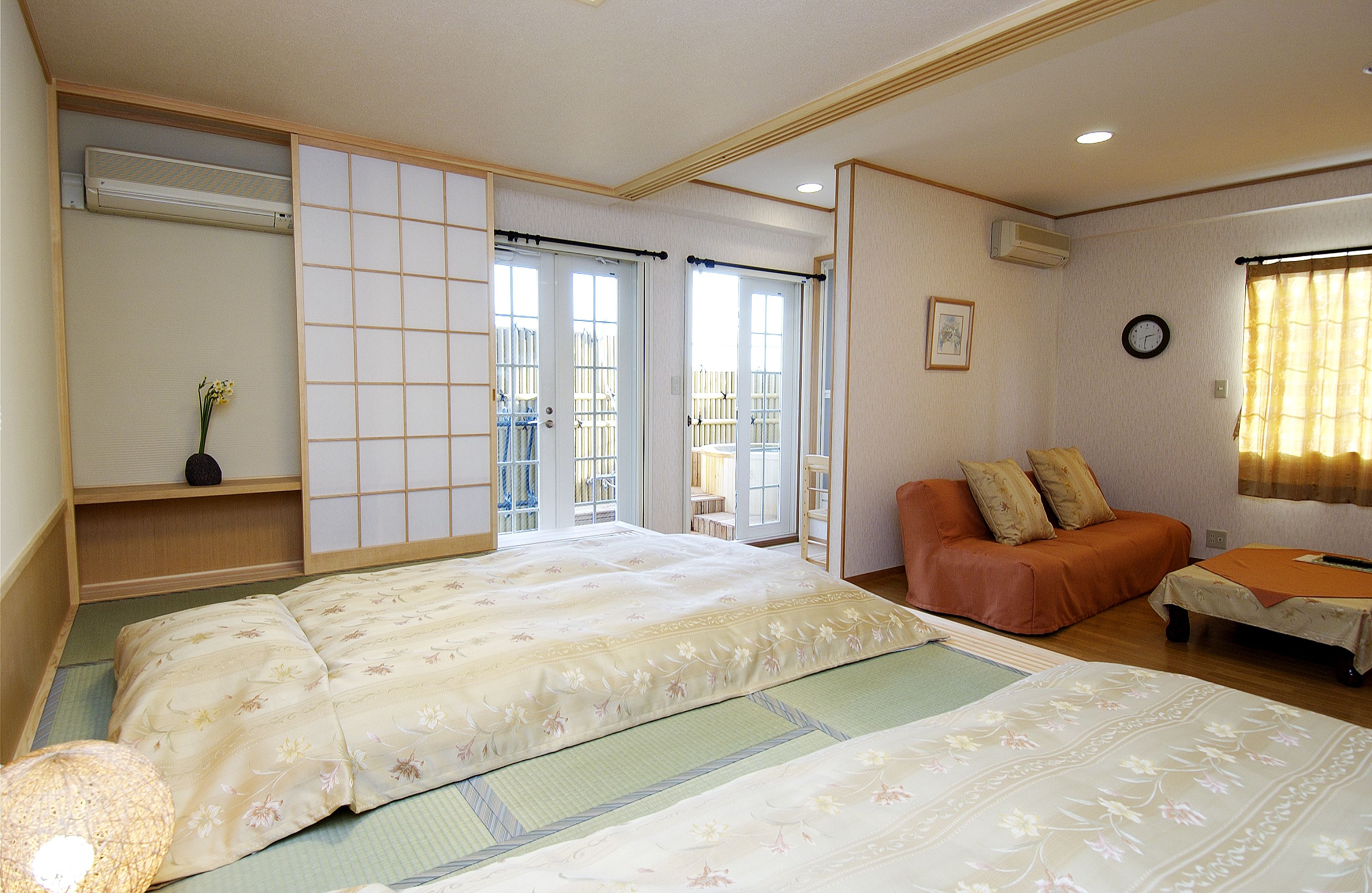 A traditional Japanese-style bedroom with tatami flooring, a low bed, a sofa, and sliding doors leading to a balcony.
