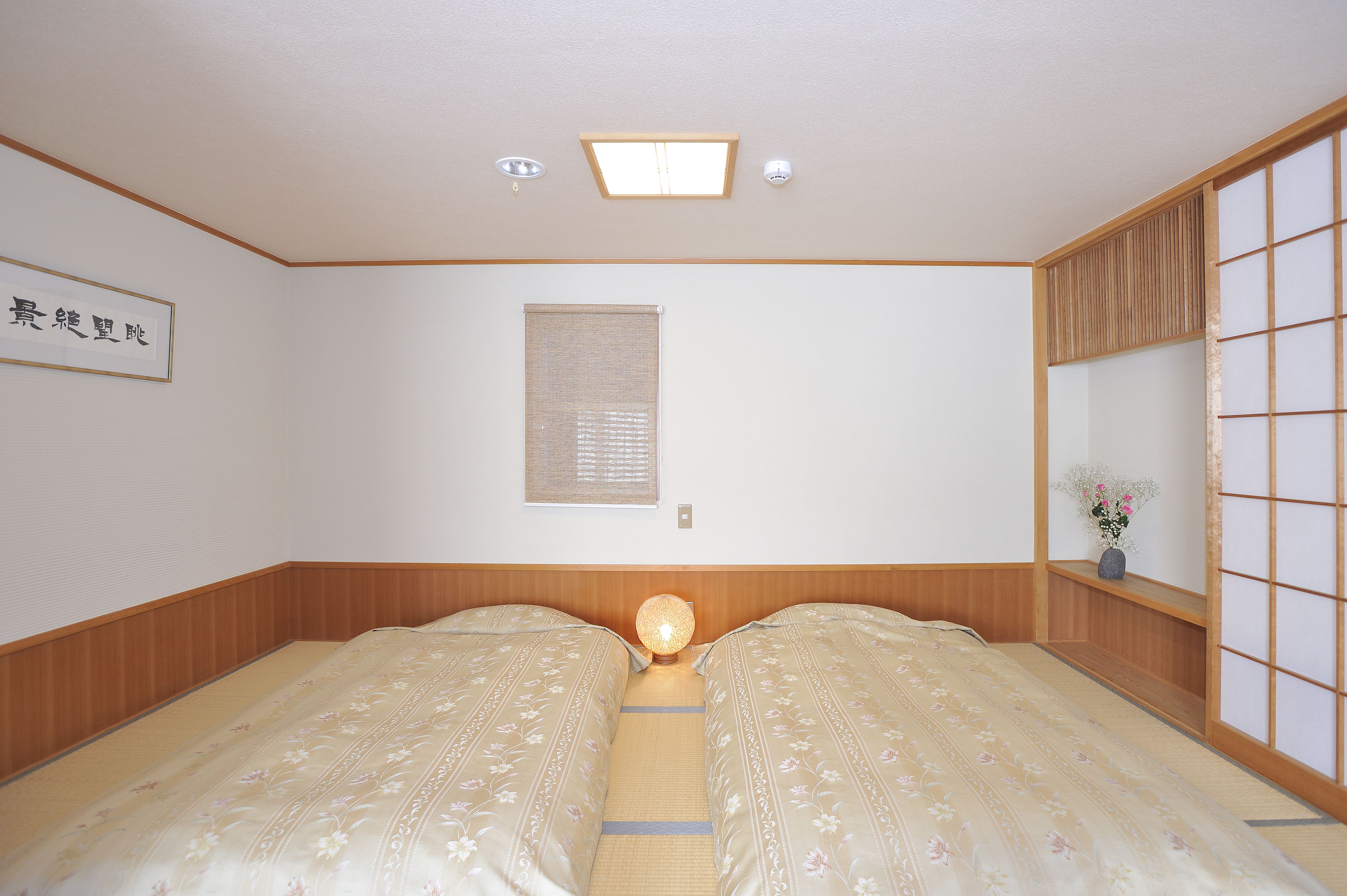 Um quarto japonês tradicional com tatames, futon e um ecrã shoji, além de uma luminária no teto.