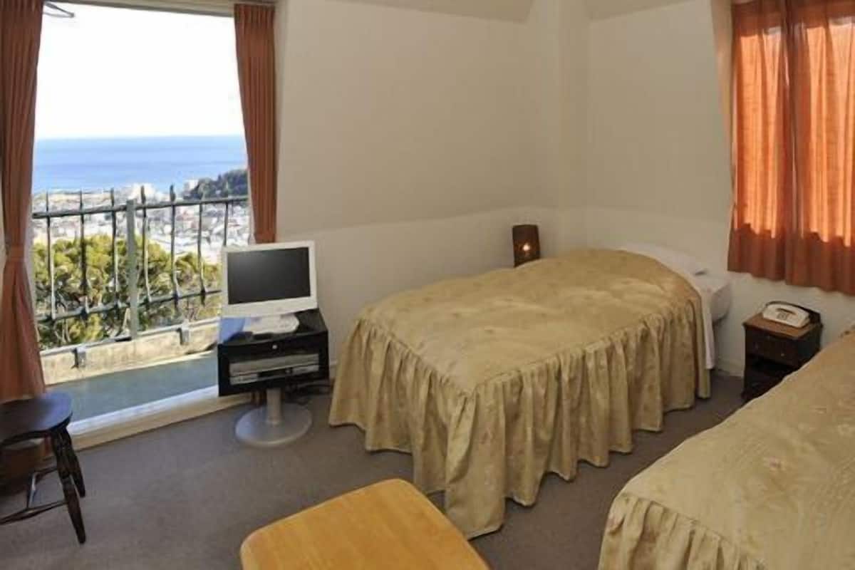 A hotel room with two beds, a television, a desk, and a view of the sea.