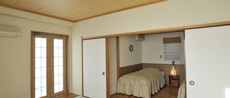 A traditional Japanese room with tatami flooring, a low table with a white tablecloth, a bed with a floral bedspread, and sliding doors.