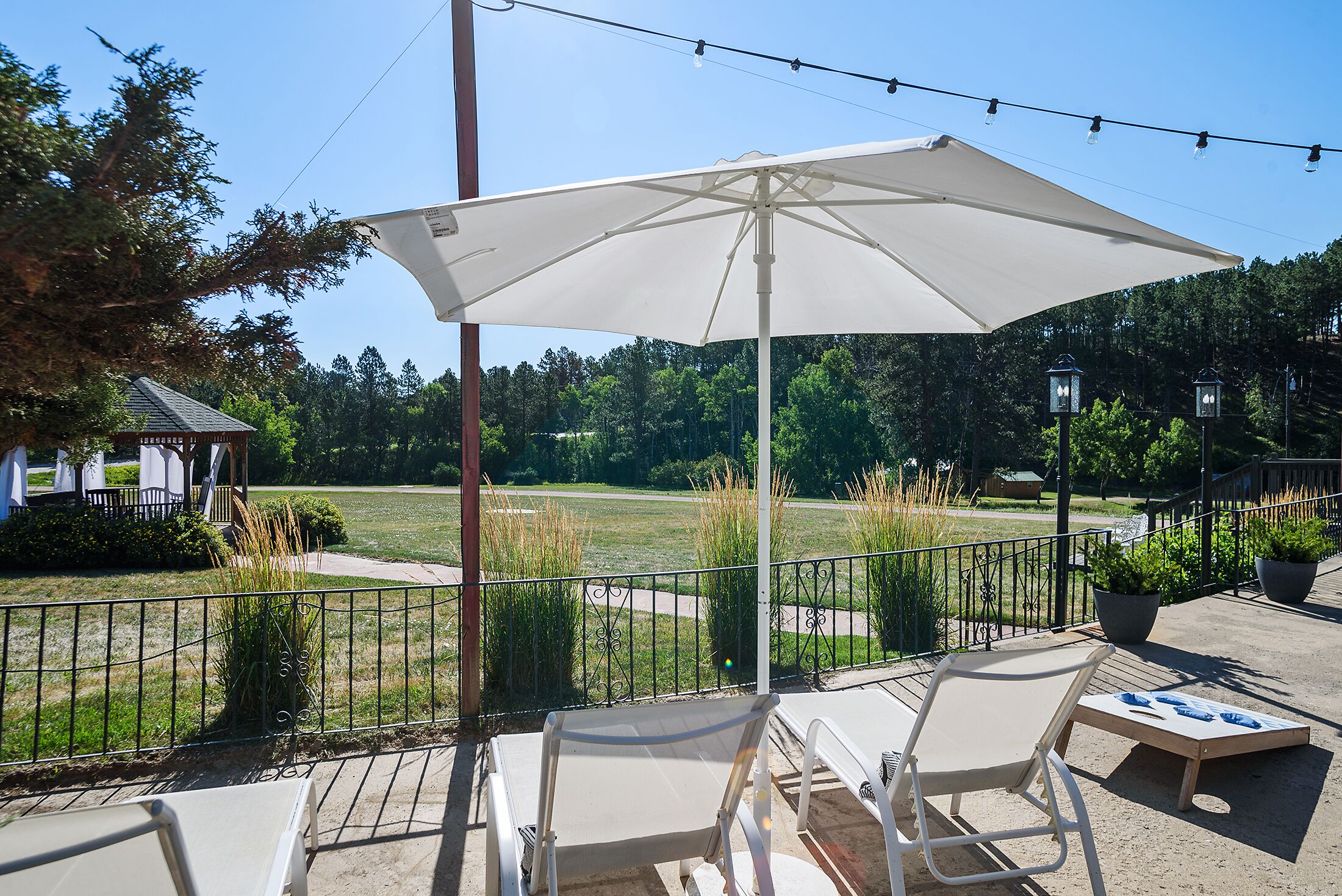 Een terras buiten met een grote parasol, twee loungestoelen en uitzicht op een grasveld en bomen.