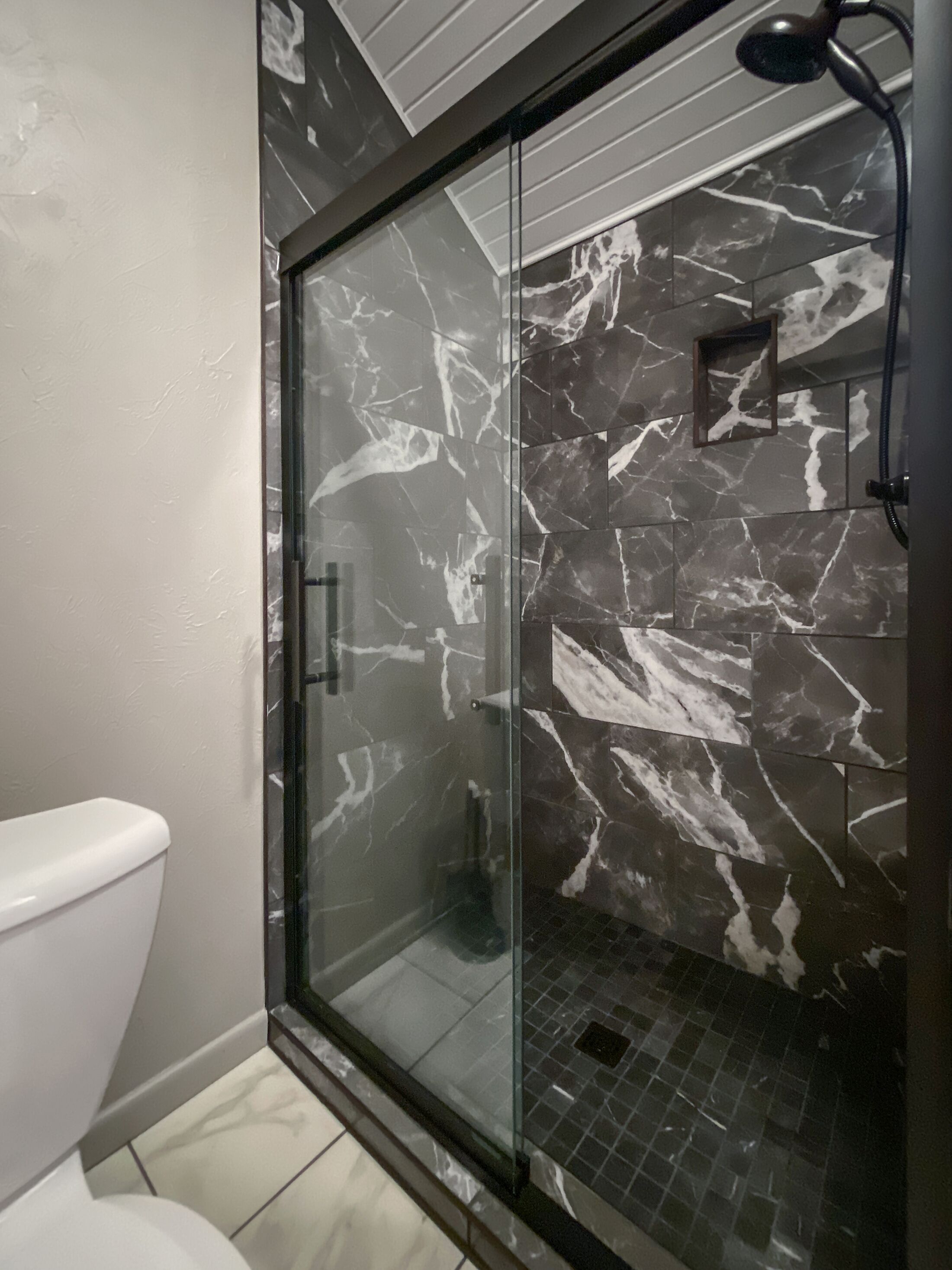 Un baño con cabina de ducha de vidrio, inodoro y suelo de baldosas.