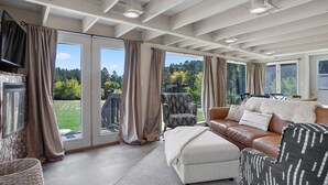 A spacious living room with a large sliding glass door leading to a balcony, a brown leather sofa, a patterned armchair, and a television on the wall. - Black Forest Inn Bed & Breakfast (Rapid City)