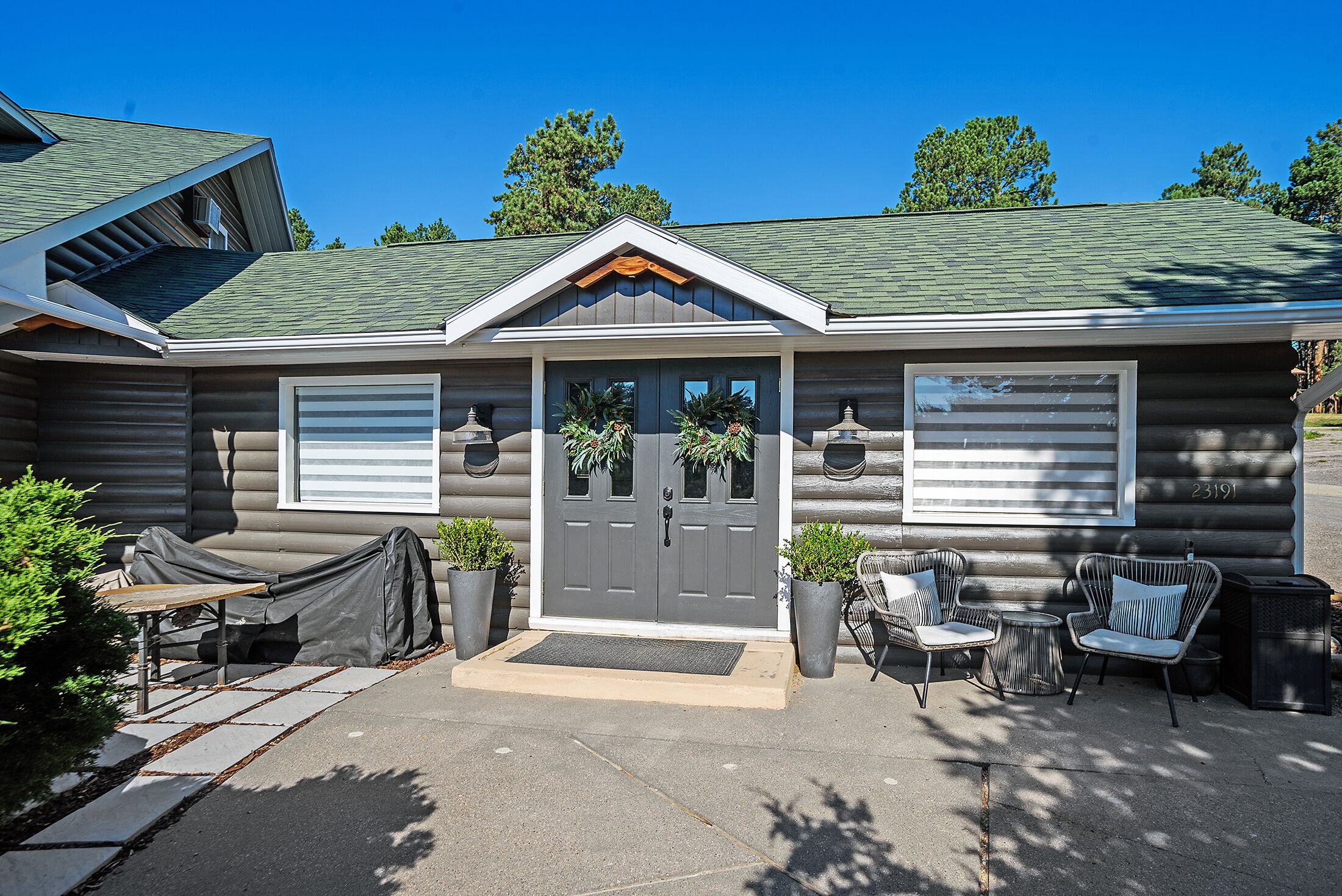 A log cabin with a front porch, two garage doors, and outdoor seating.