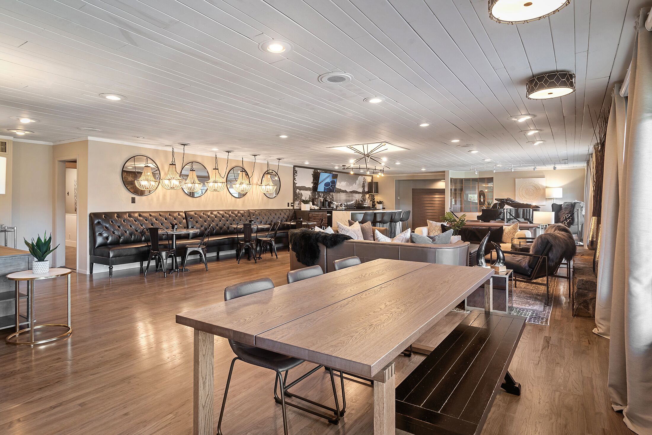A spacious dining area with a long wooden table and multiple chairs, a leather sofa, and a television mounted on the wall.