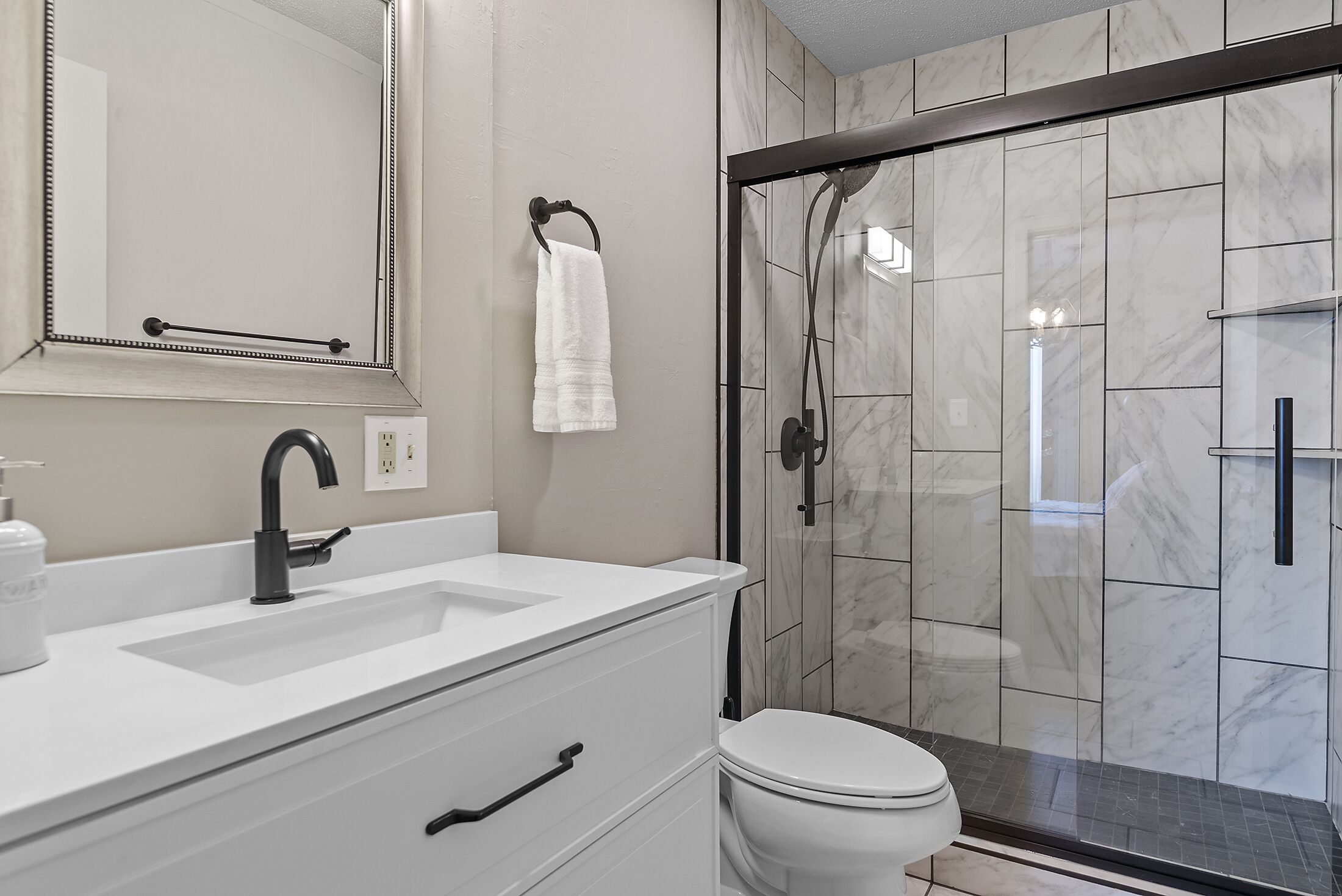 Une salle de bain moderne avec un lavabo blanc, un robinet noir et une cabine de douche en verre.