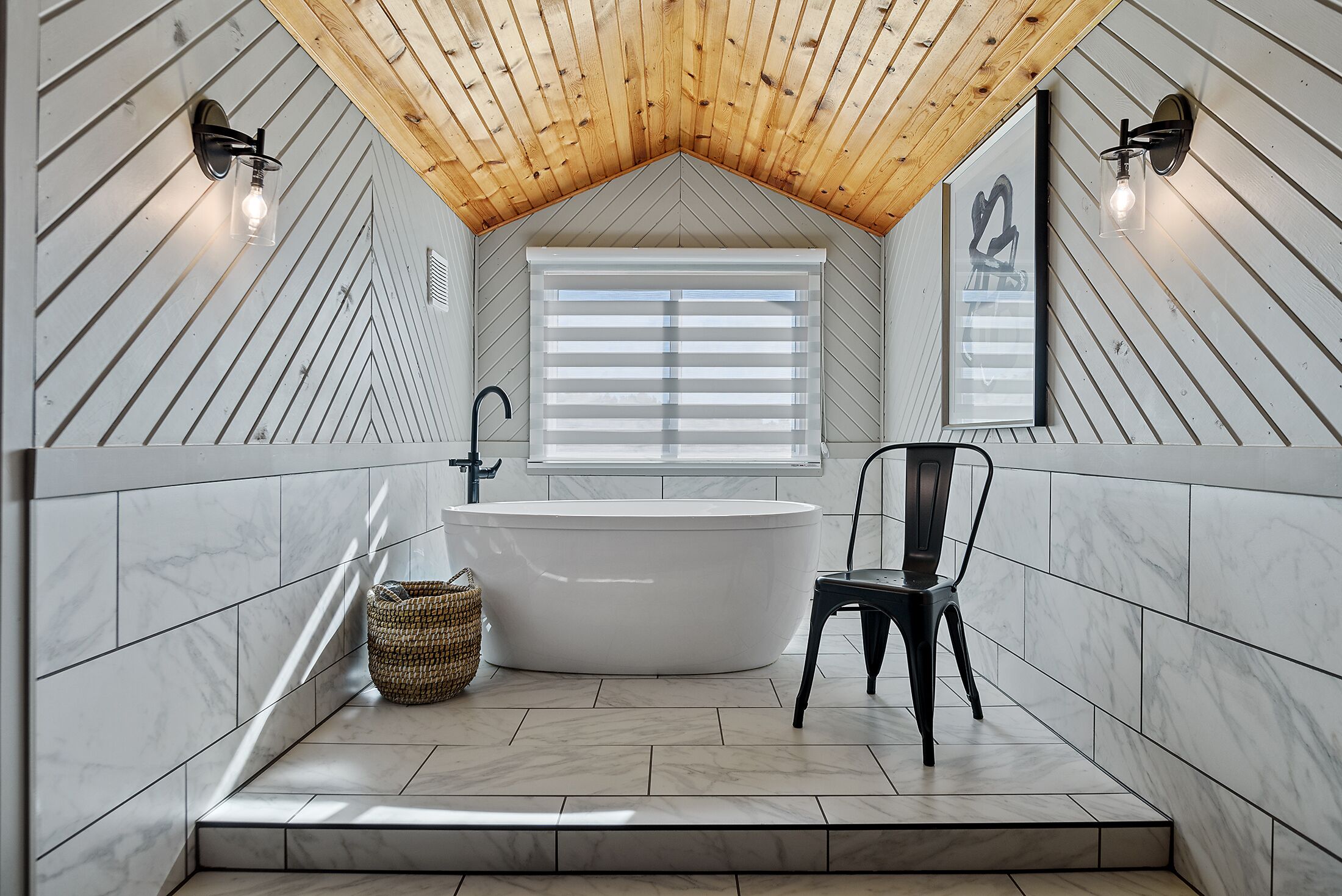 A modern bathroom with a freestanding bathtub, a wooden ceiling, and a window with blinds.