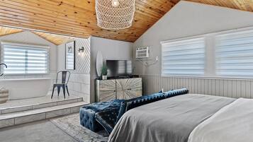 A bedroom with a large bed, a wooden ceiling, a TV, and a window with blinds.
