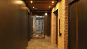 A narrow, well-lit corridor with tiled flooring and wooden panel ceilings. - HOTEL AMANEK Ginza East (Tokyo)