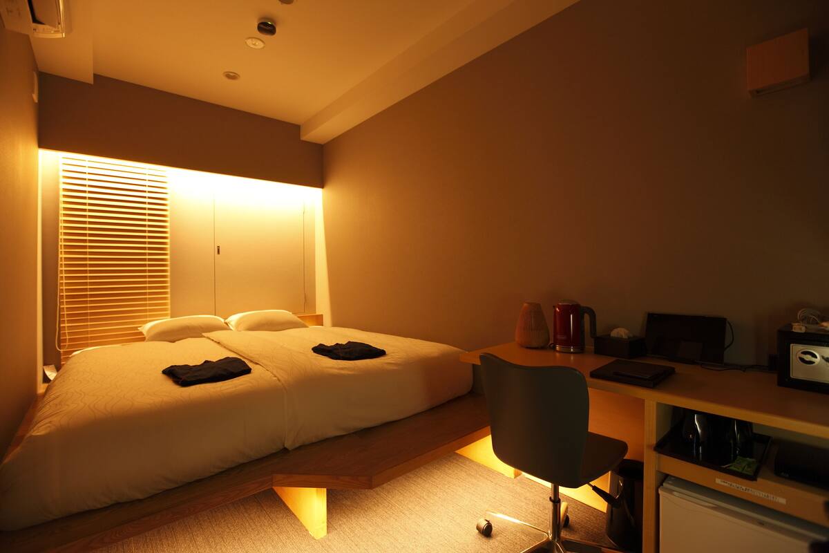 A hotel room with a bed, desk, chair, and a small kitchenette.