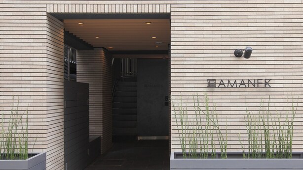 A modern building entrance with a staircase leading inside, a nameplate on the wall, and two planters with greenery. - HOTEL AMANEK Ginza East (Tokyo)