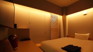 A hotel room with a bed, a nightstand, a lamp, a trash bin, and a window with blinds. - HOTEL AMANEK Ginza East (Tokyo)