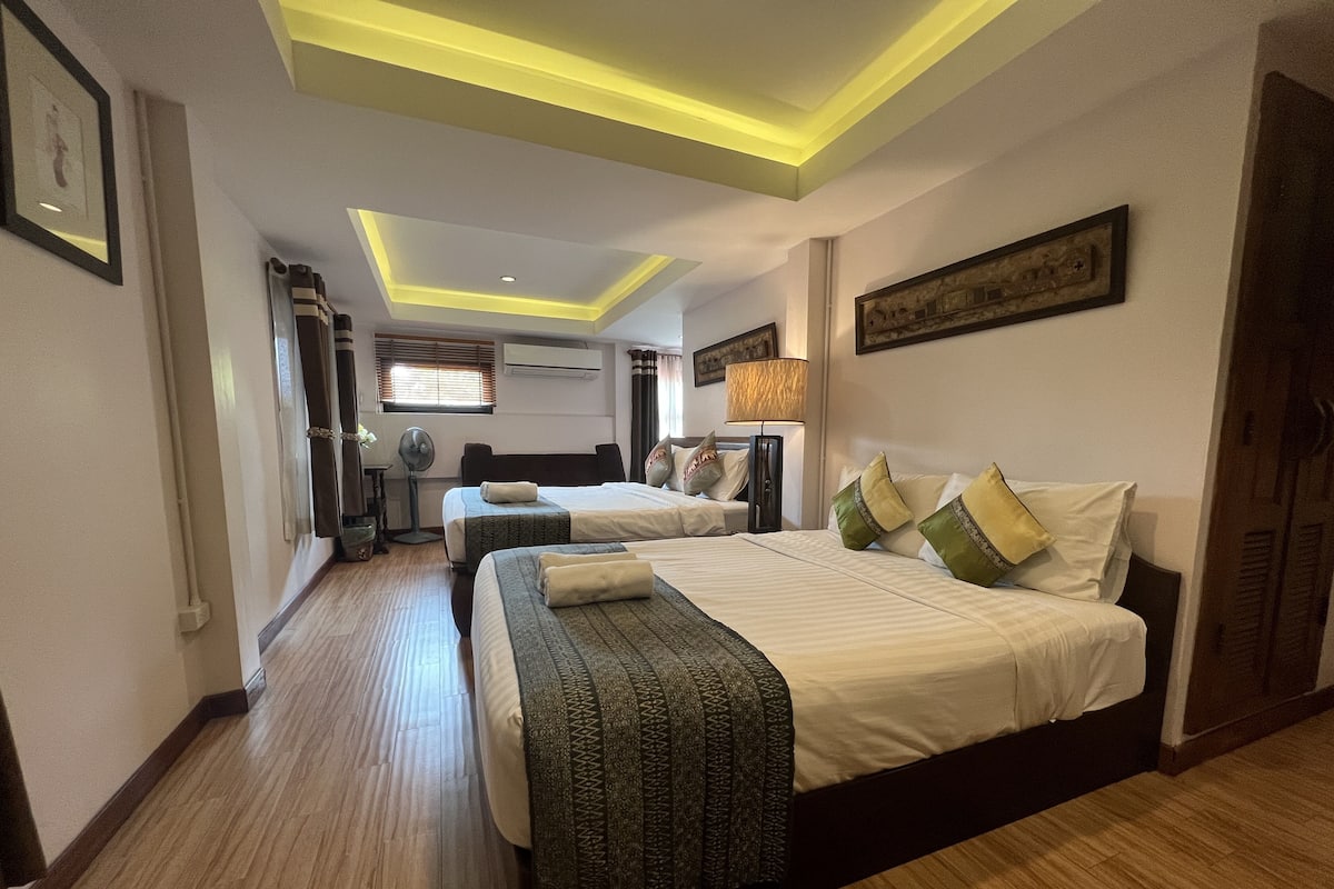 Een hotelkamer met twee bedden, een plafondventilator, een airconditioning en een raam met jaloezieën.