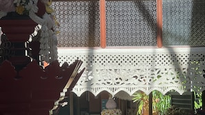 Un patio interior con un banco de madera, una mesa decorativa con flores y una ventana con encaje.