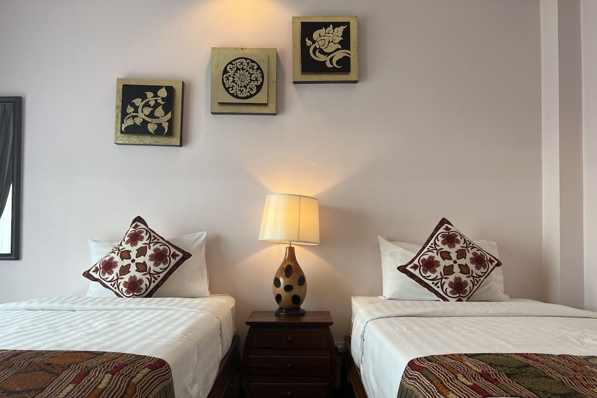 Hotelkamer met twee bedden, elk voorzien van een gestreept kussen, een nachtkastje met een lamp en drie decoratieve objecten aan de muur.