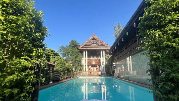 Una piscina con vistas a un edificio tradicional de techo triangular y columnas.