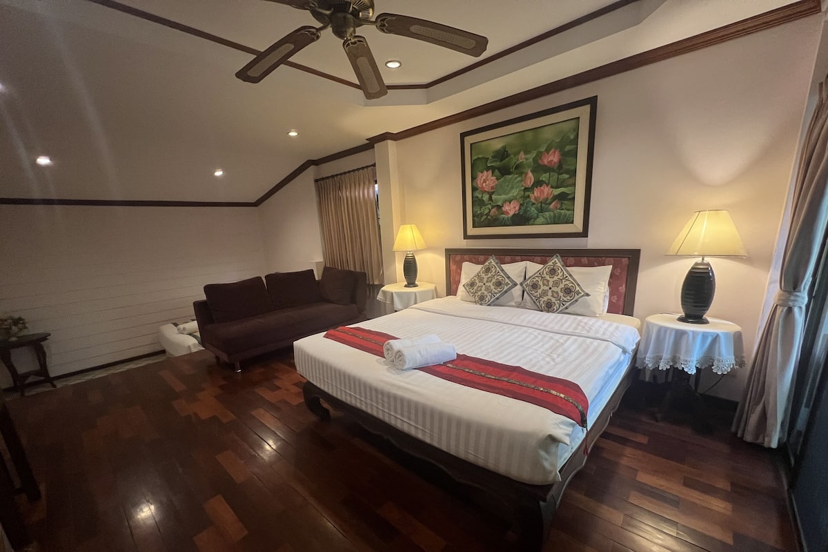 Een hotelkamer met een groot bed, een slaapbank, een plafondventilator en een schilderij aan de muur.