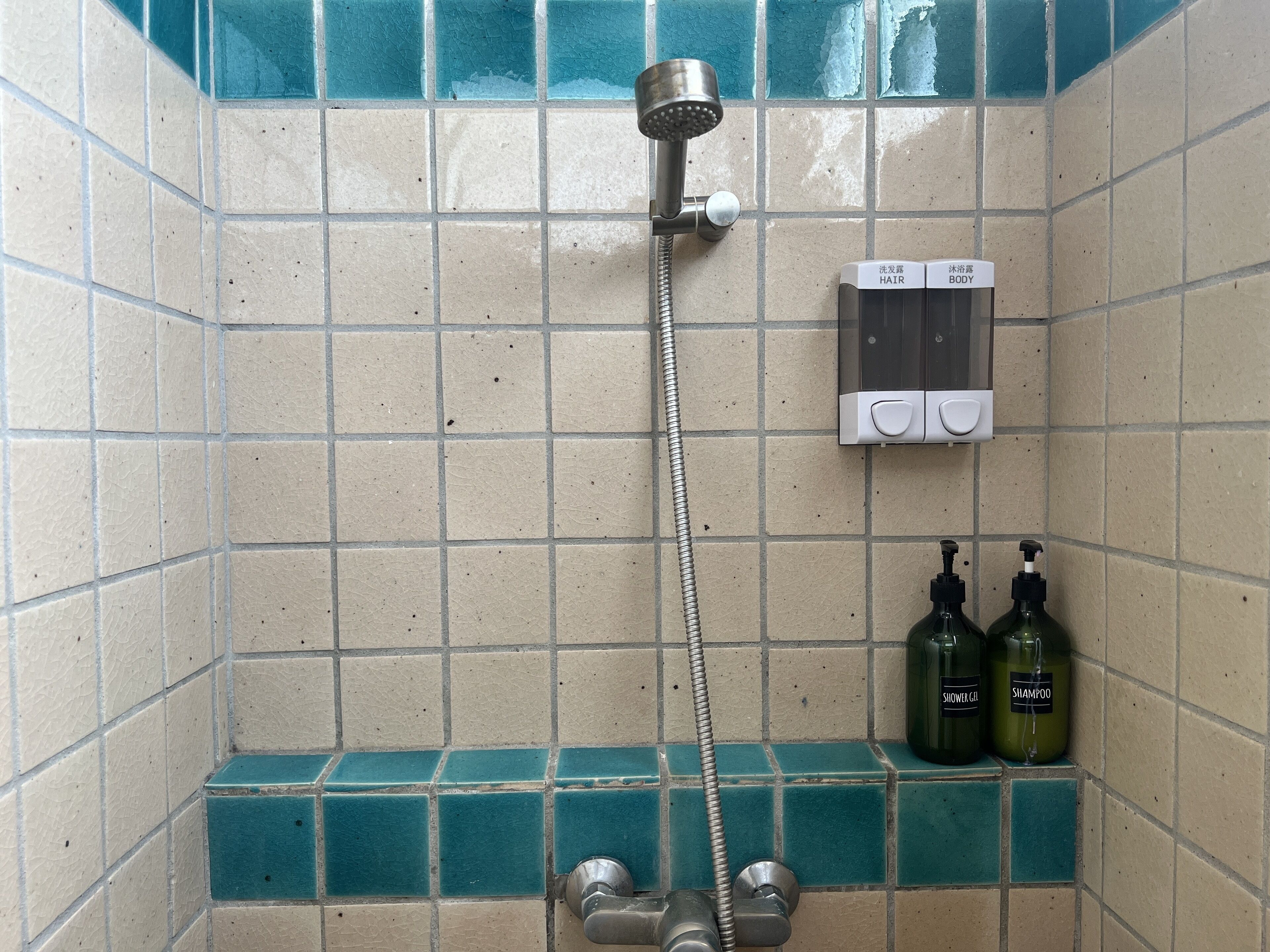 Un baño con ducha, dispensador de jabón y dos botellas de champú.