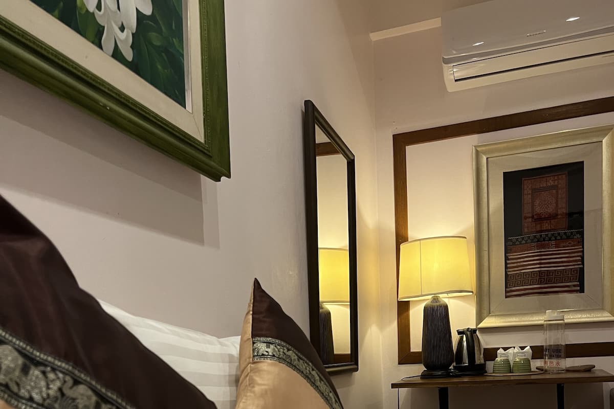 Een hotelkamer met een opgemaakt bed, een nachtkastje met een lamp, een spiegel en een lijst met een afbeelding aan de muur.