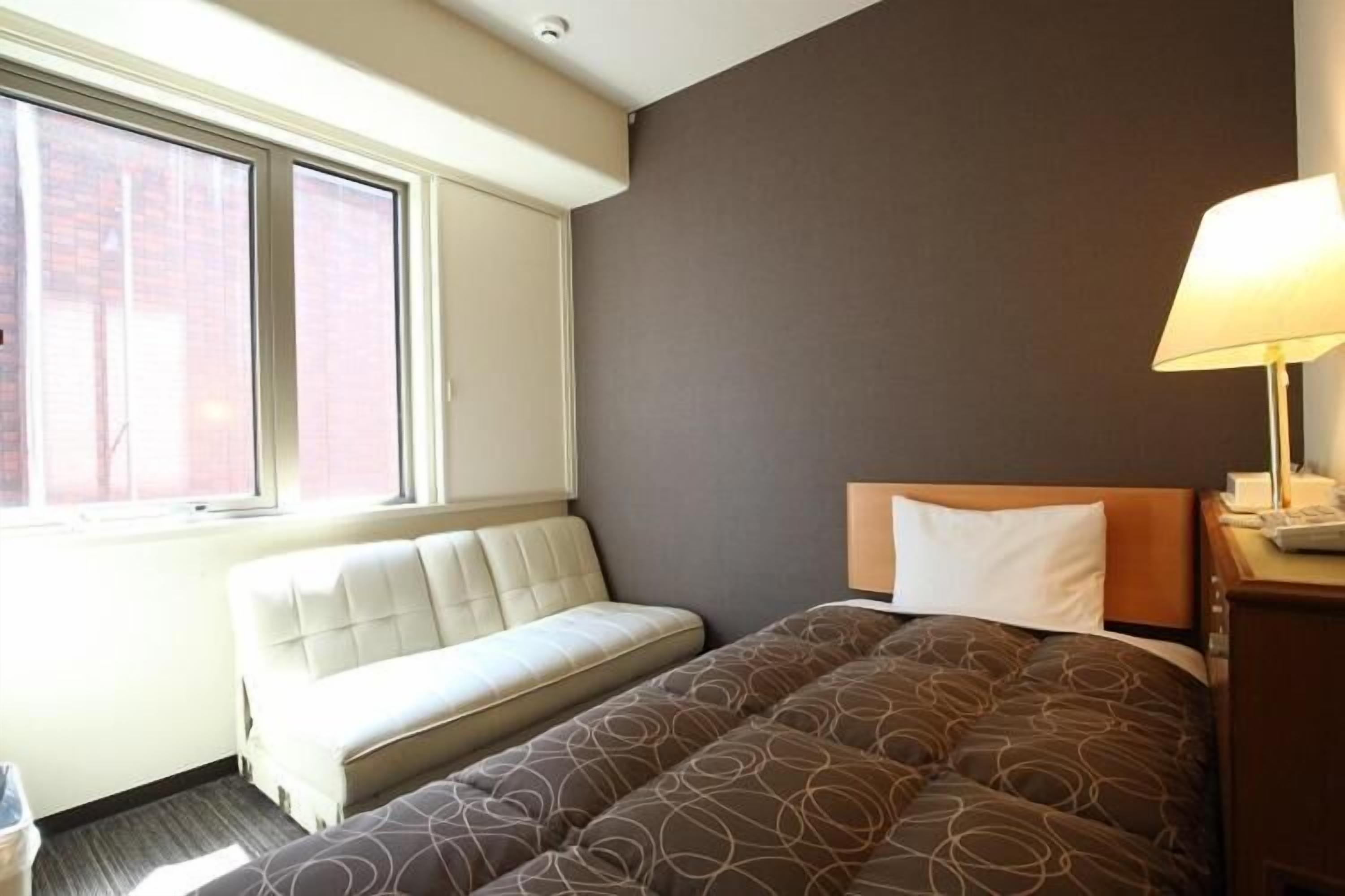 Una habitación de hotel con cama, sofá, ventana y lámpara.