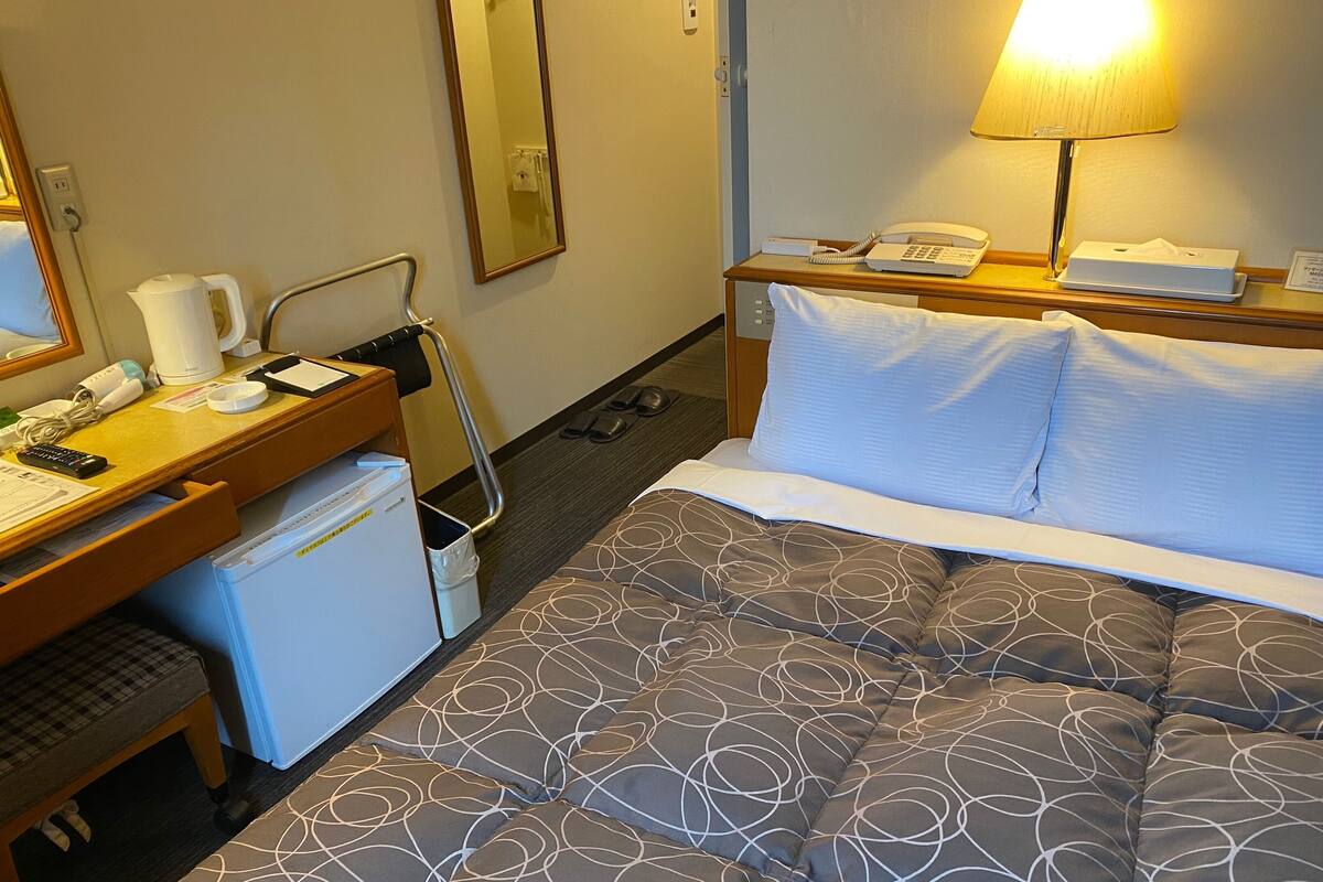 Ein Hotelzimmer mit Bett, Schreibtisch mit Lampe, Telefon, Kaffeemaschine und kleinem Kühlschrank.