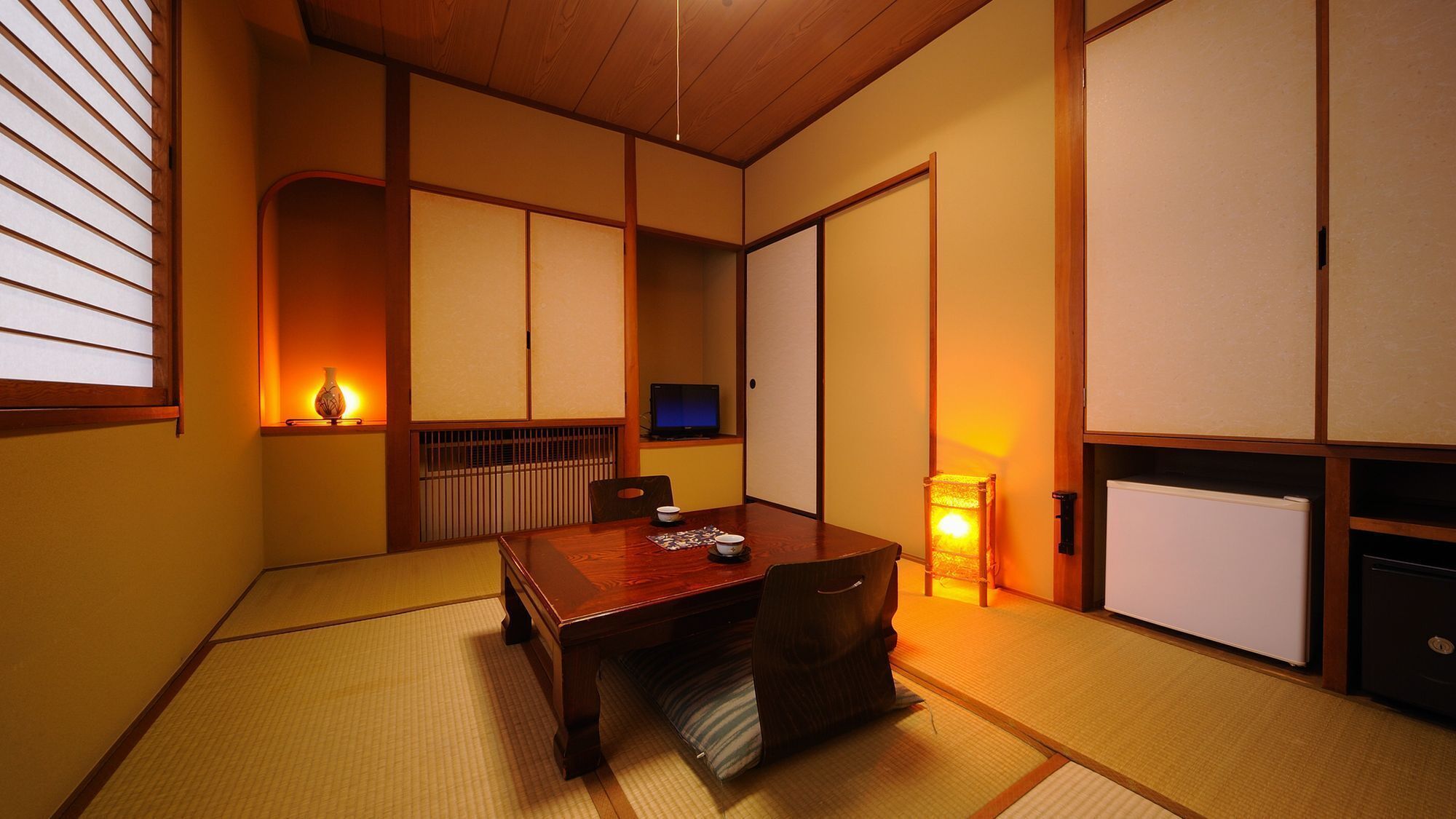 A traditional Japanese room with tatami flooring, a low table, sliding doors, and a television.