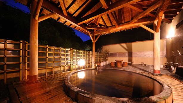 Un área de aguas termales al aire libre con madera, que incluye una terraza de madera y un baño termal circular.