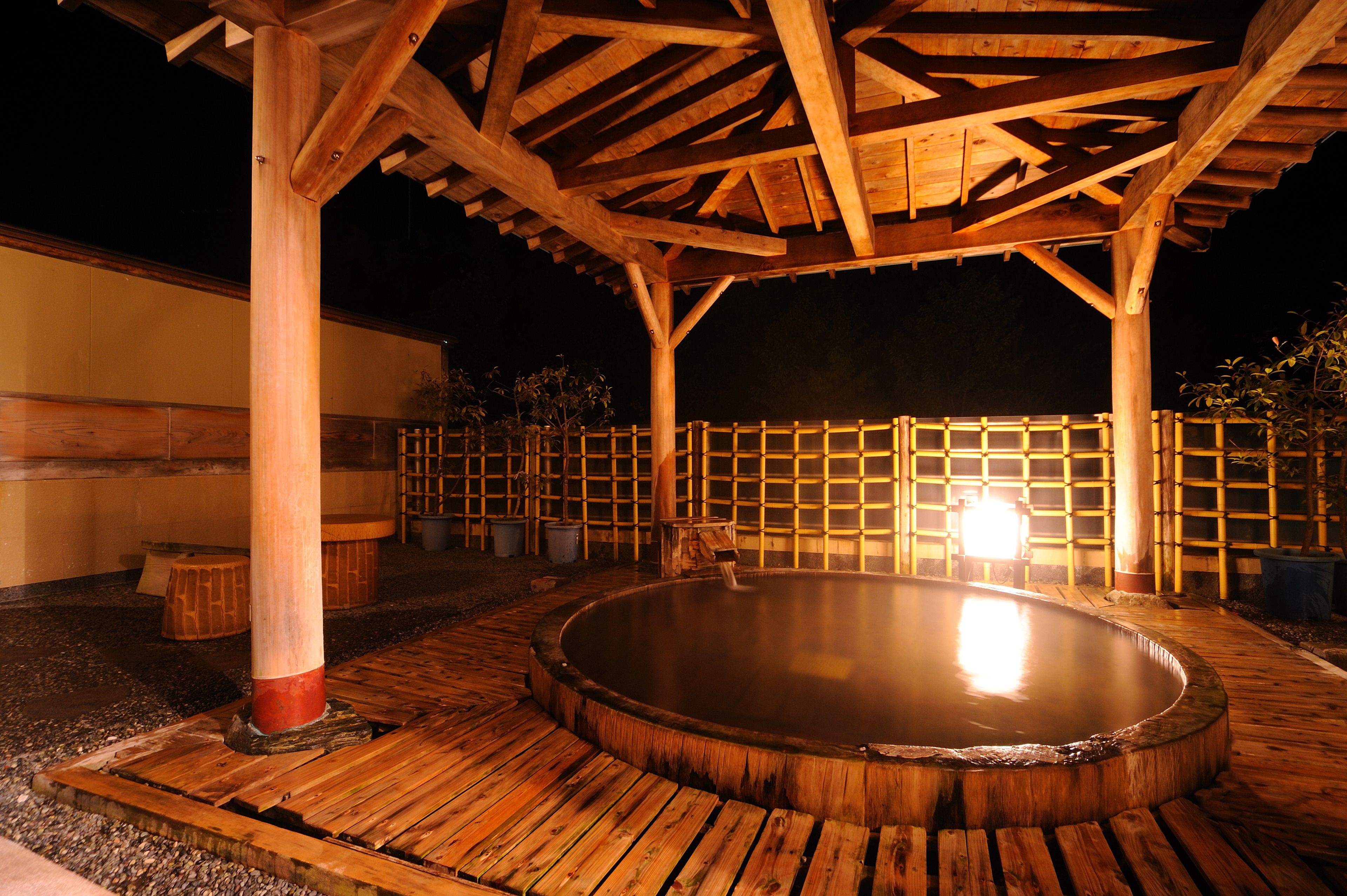 A wooden hot tub under a wooden pergola at night.