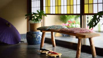 A wooden bench with cushions, a purple umbrella, and potted plants in a room with a tiled floor and a window with a grid pattern.