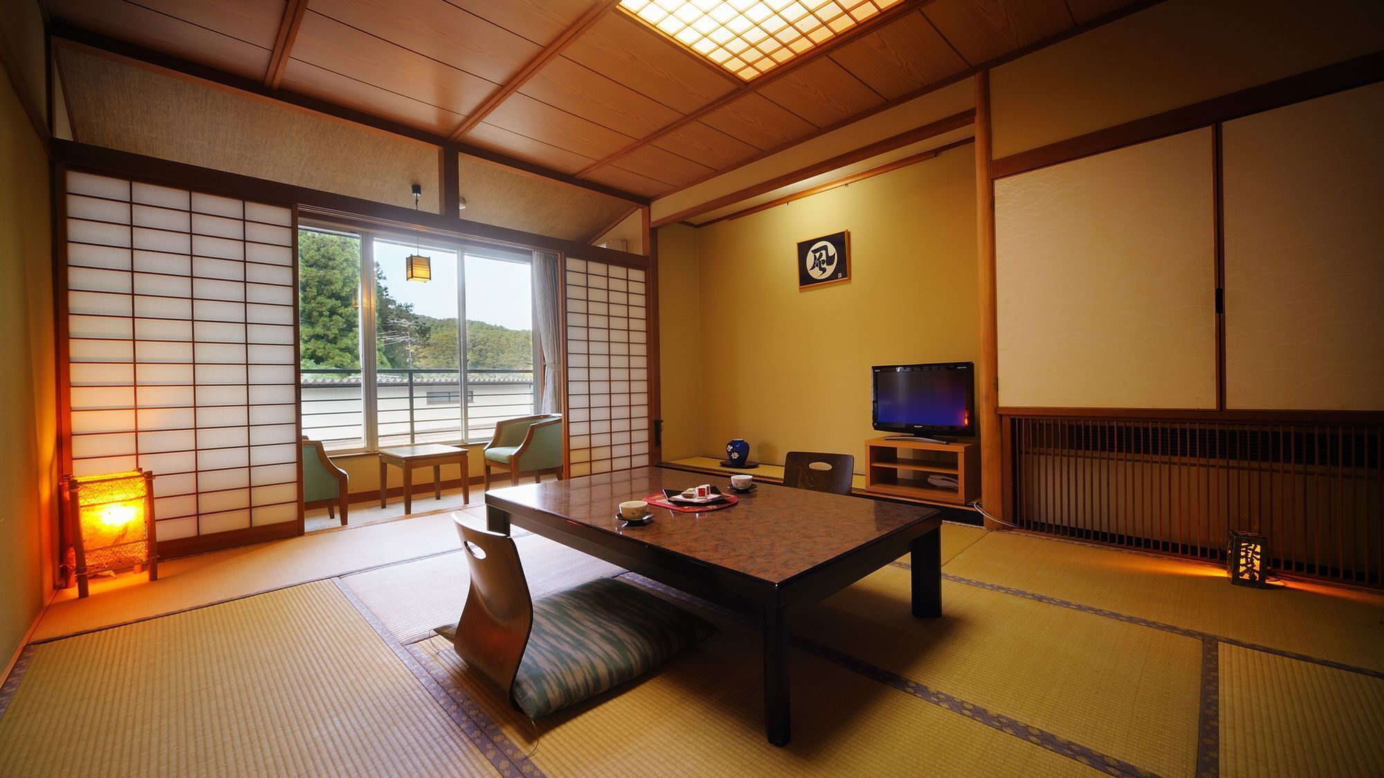 A traditional Japanese room with tatami flooring, a low table, chairs, a television, and a sliding door with a view.