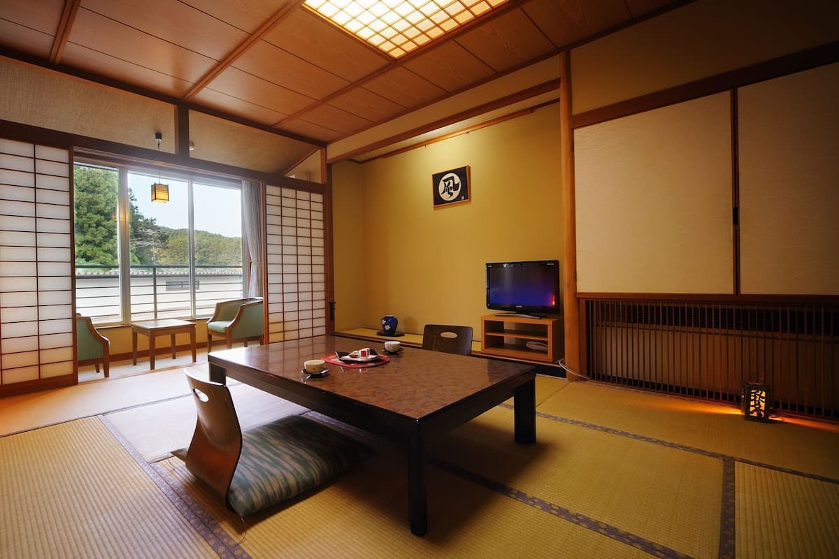 Perinteinen japanilainen huone, jossa on tatamimatto, matala pöytä, tuoleja, televisio ja liukuovi, josta on näkymä ulos.