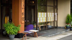 Un edificio japonés tradicional con entrada de madera, una planta en maceta y una pequeña mesa con cojín.
