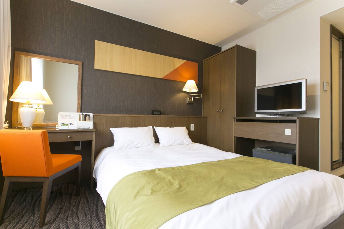A hotel room with a bed, a desk, a chair, a television, and a mirror.