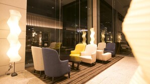 Un vestíbulo moderno con una zona de estar que incluye una variedad de sillones y sofás, una alfombra estampada y un amplio ventanal con vistas a la ciudad.