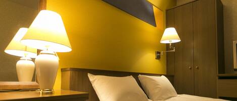 Quarto de hotel com cama, duas luminárias de cabeceira, um painel de cabeceira de madeira e um guarda-roupa.