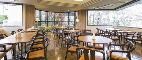 A spacious dining area with multiple tables and chairs, large windows offering views of the outside, and a modern ceiling design.