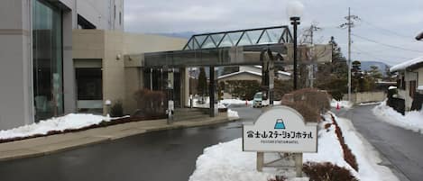 A FUJISAMI STATION HOTEL sign in front of a building with a glass entrance and a snow-covered sidewalk.