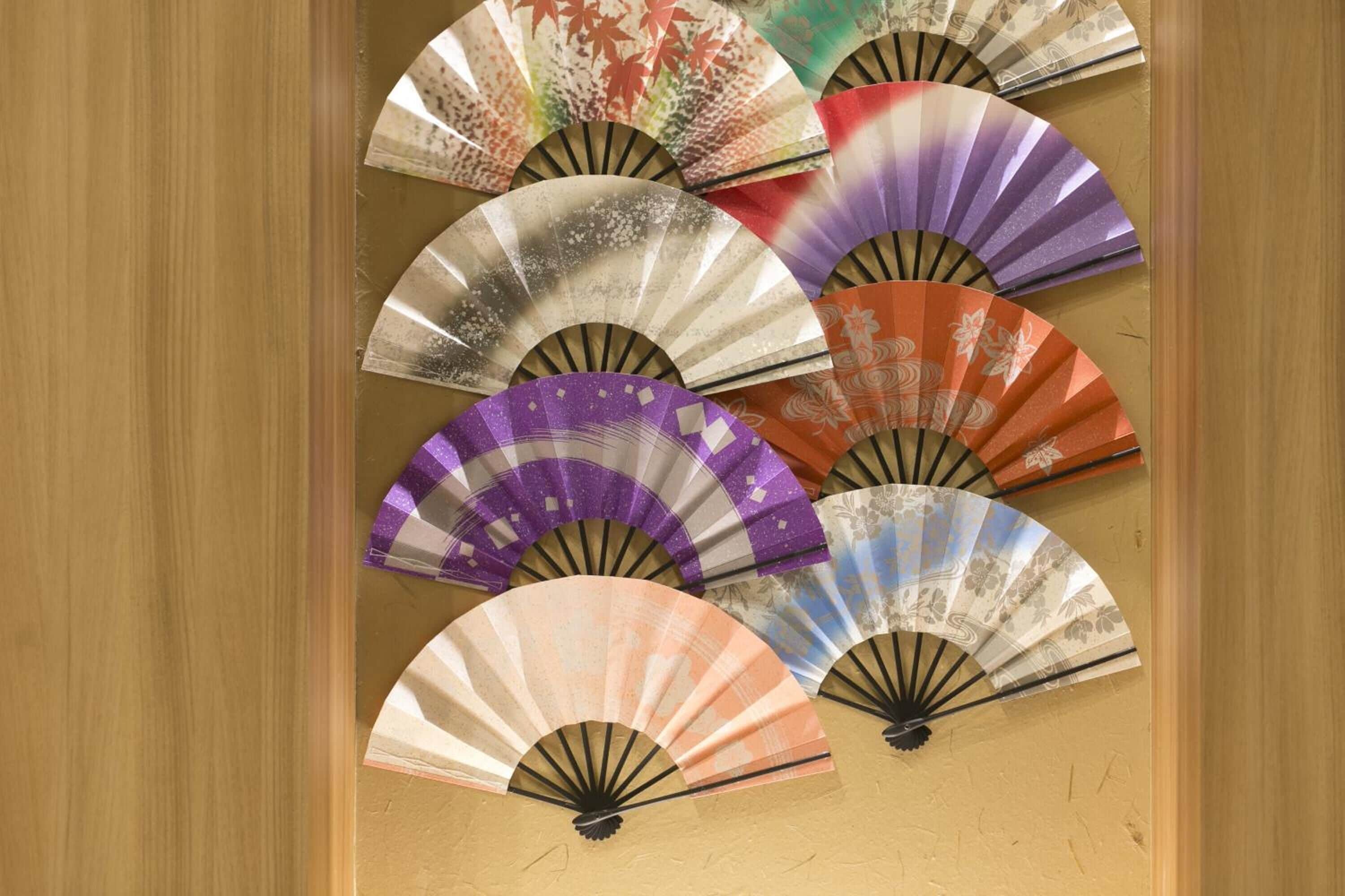 A wall with multiple traditional fans in various colors and designs.