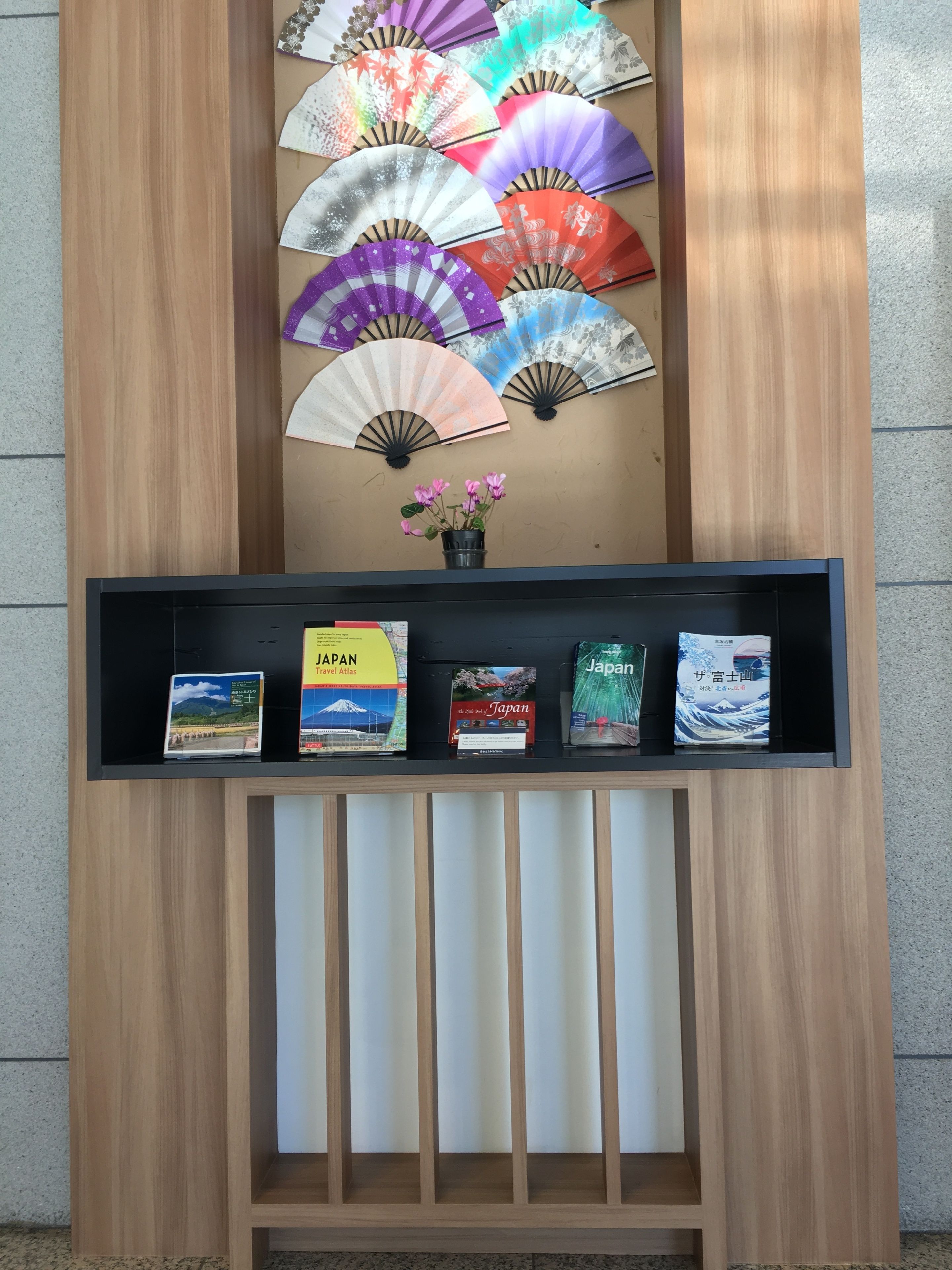 A wooden display with a shelf of travel books and a wall decorated with traditional Japanese fans.
