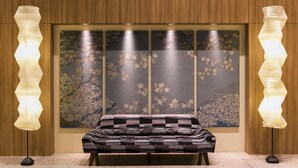 Habitación con sofá frente a una pared con estampado floral y dos lámparas de pie a cada lado.