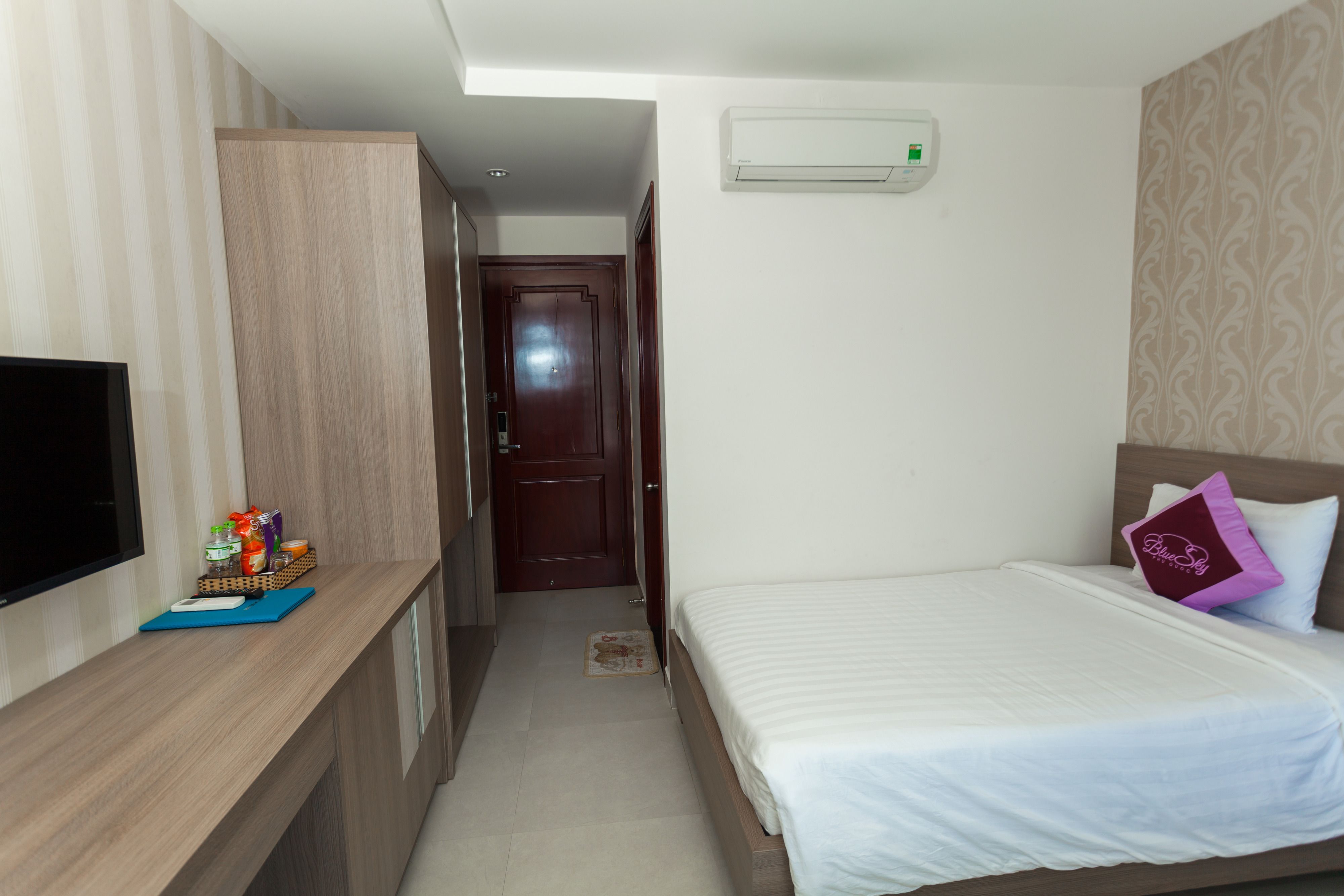 A hotel room with a bed, a TV, a desk with a keyboard and mouse, and an air conditioning unit.