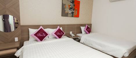 A hotel room with two beds, each with white bedding and pink pillows, a mirror, a painting on the wall, and an air conditioning unit.