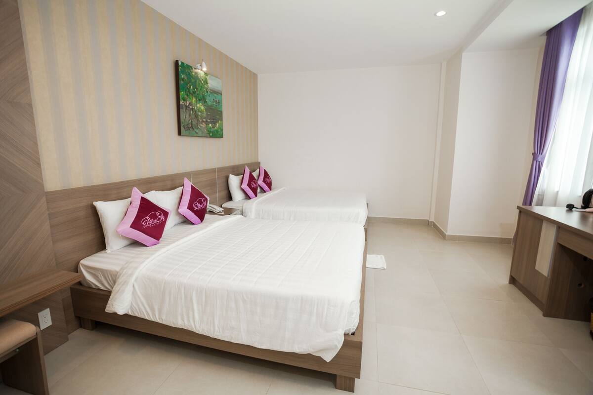 A hotel room with two beds, a desk, and a painting on the wall.