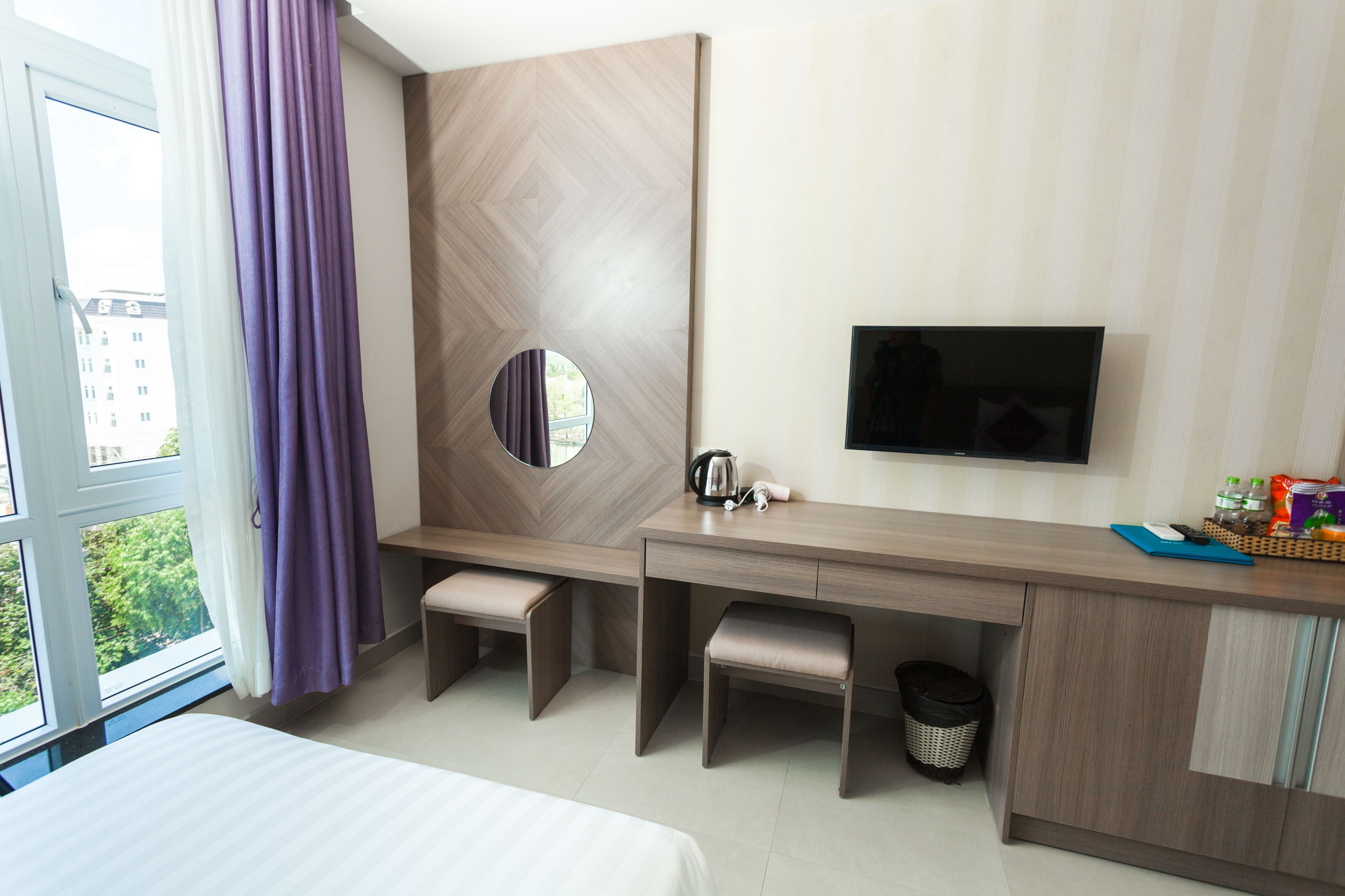 A hotel room with a bed, a desk with a chair, a television, and a window with curtains.