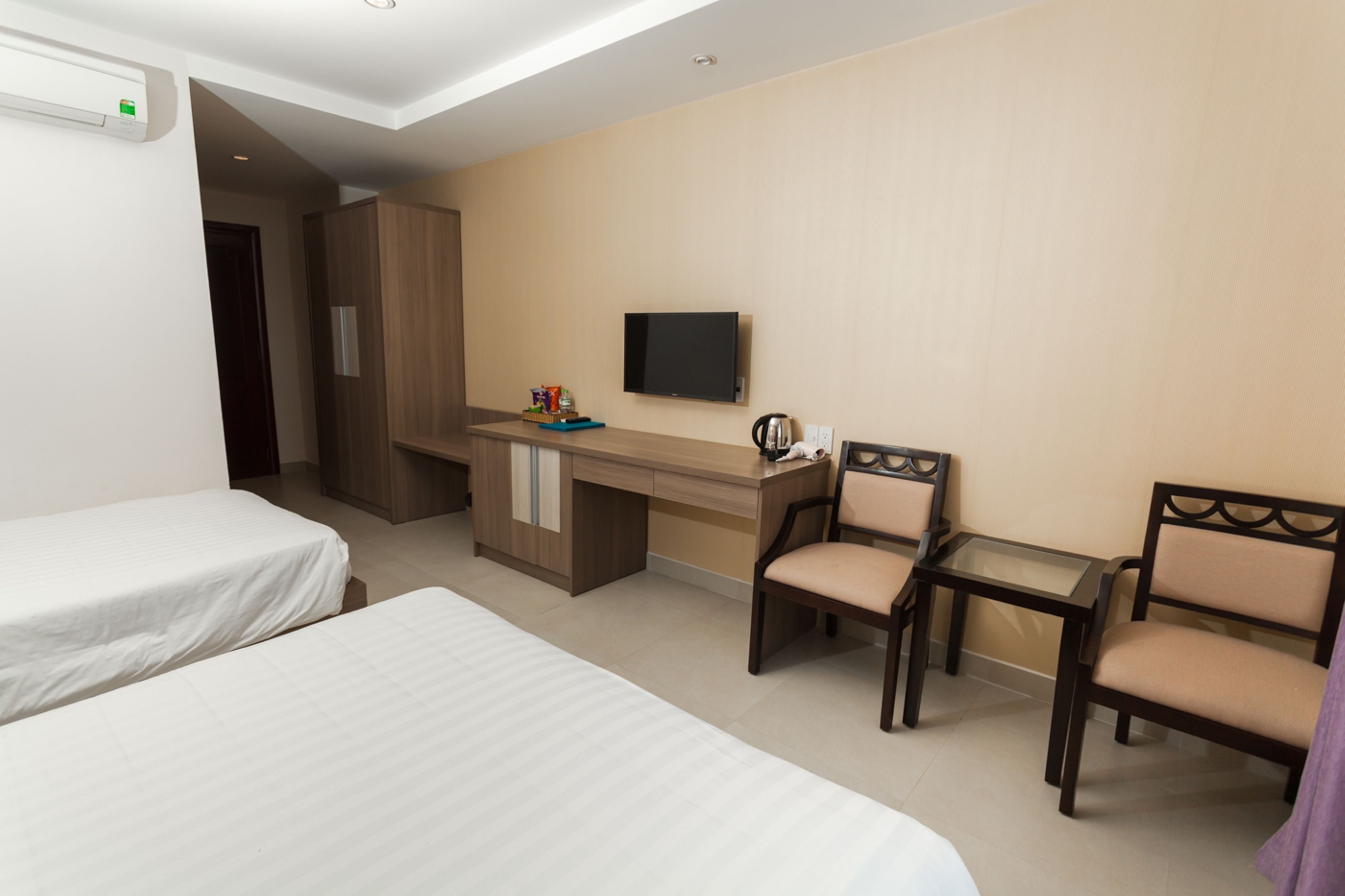 A hotel room with two single beds, a desk with a chair, a television, and a small table.