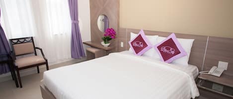 Habitación de hotel con una cama grande, una mesita de noche con teléfono, una silla y una pequeña mesa con un florero.