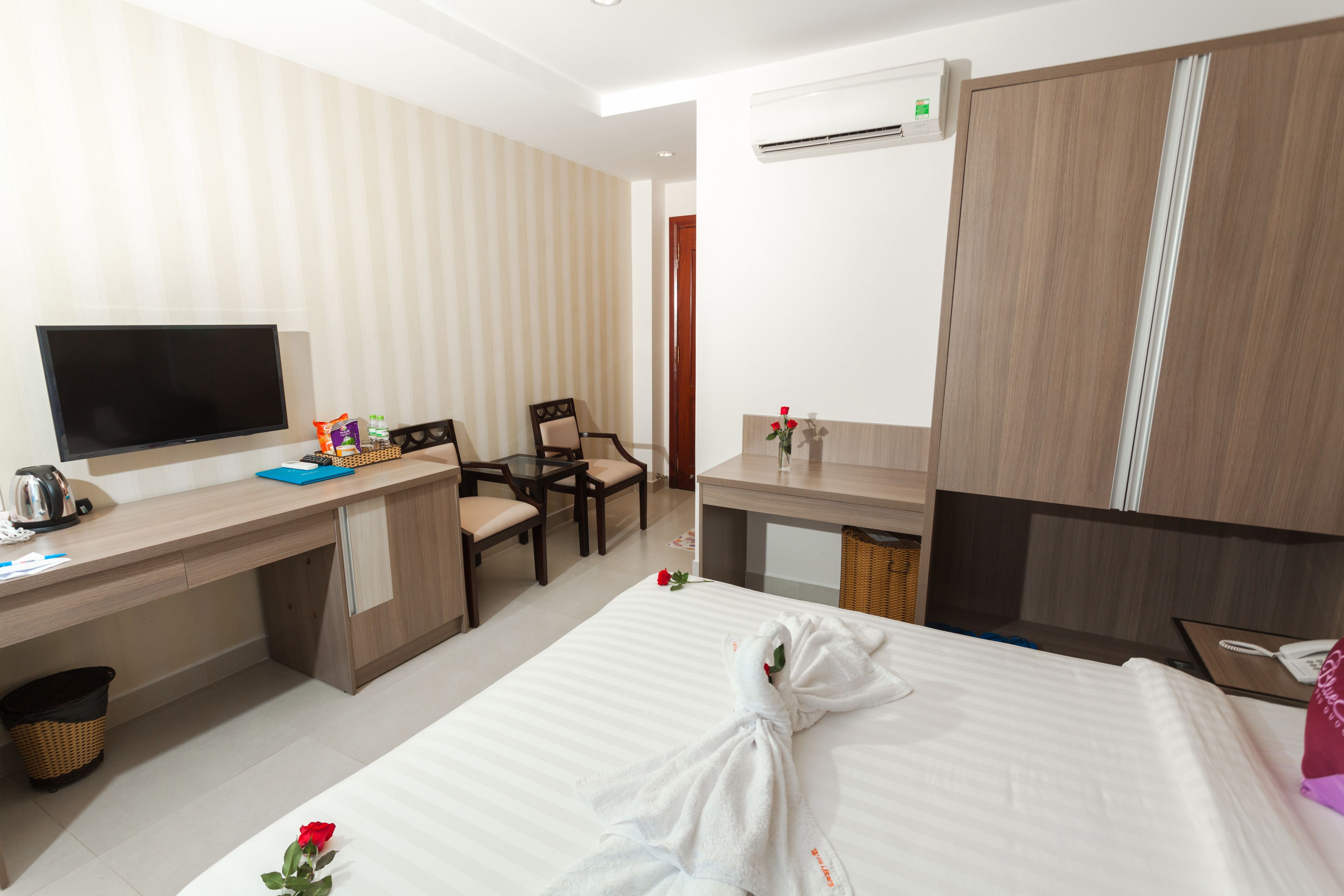 Quarto de hotel com cama, escrivaninha com televisão, cadeira e pequena mesa com um vaso de flores.
