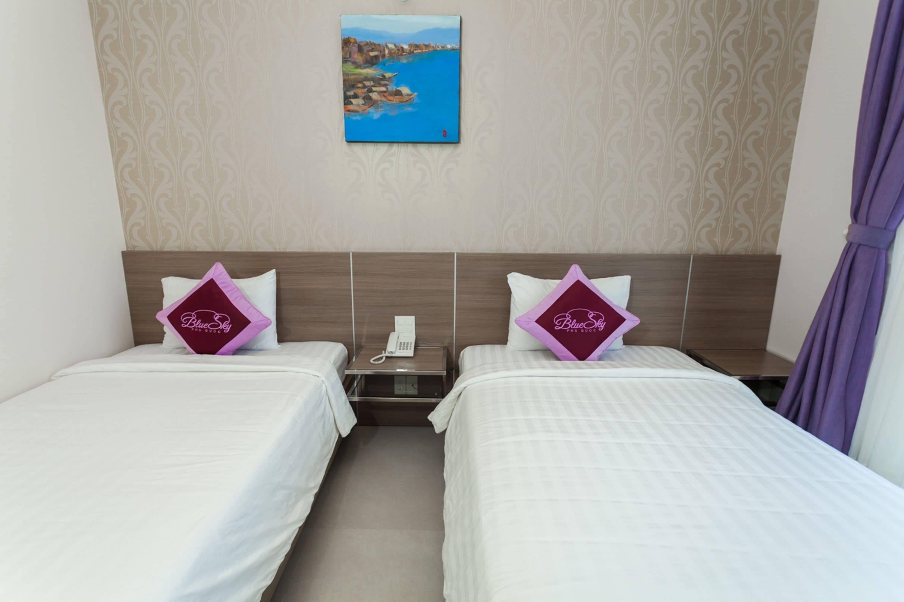 A hotel room with two beds, a painting on the wall, and a telephone on the nightstand.