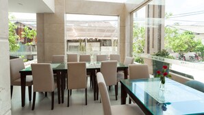 A dining area with a glass table and chairs, a vase with flowers, and a view of the street outside. - Blue Sky Phu Quoc Hotel (Phu Quoc)